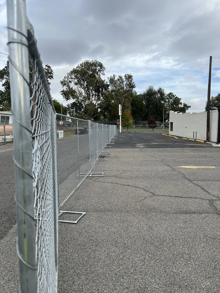 Temporary chain-link fence panels on T-stands extending across a paved Pasco project site